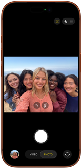 iPhone 17 Pro in Cosmic Orange, front, screen shows Center Stage front camera open with a group selfie of five people centered in frame