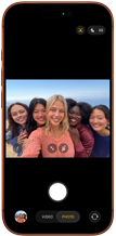 iPhone 17 Pro in Cosmic Orange, front, screen shows Center Stage front camera open with a group selfie of five people centered in frame
